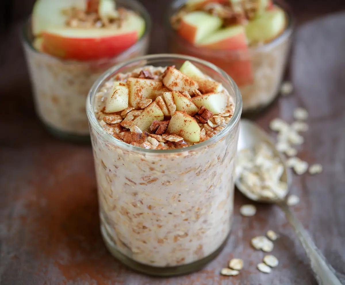 Creamy apple cinnamon protein overnight oats in a glass jar topped with apple slices and cinnamon for a healthy breakfast.