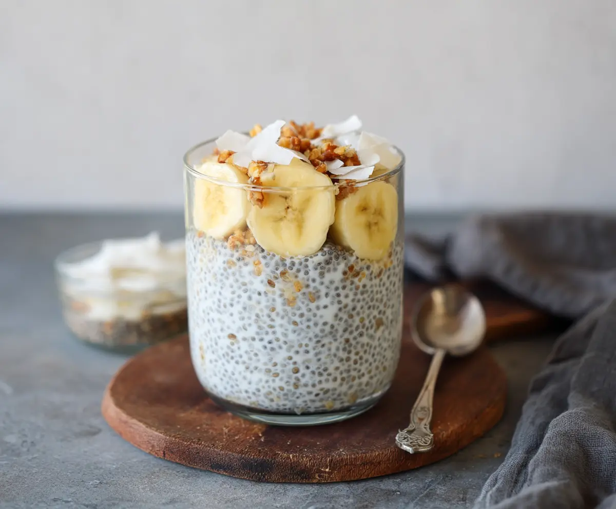 Creamy banana coconut milk chia seed pudding served in a glass bowl, topped with sliced bananas and shredded coconut.