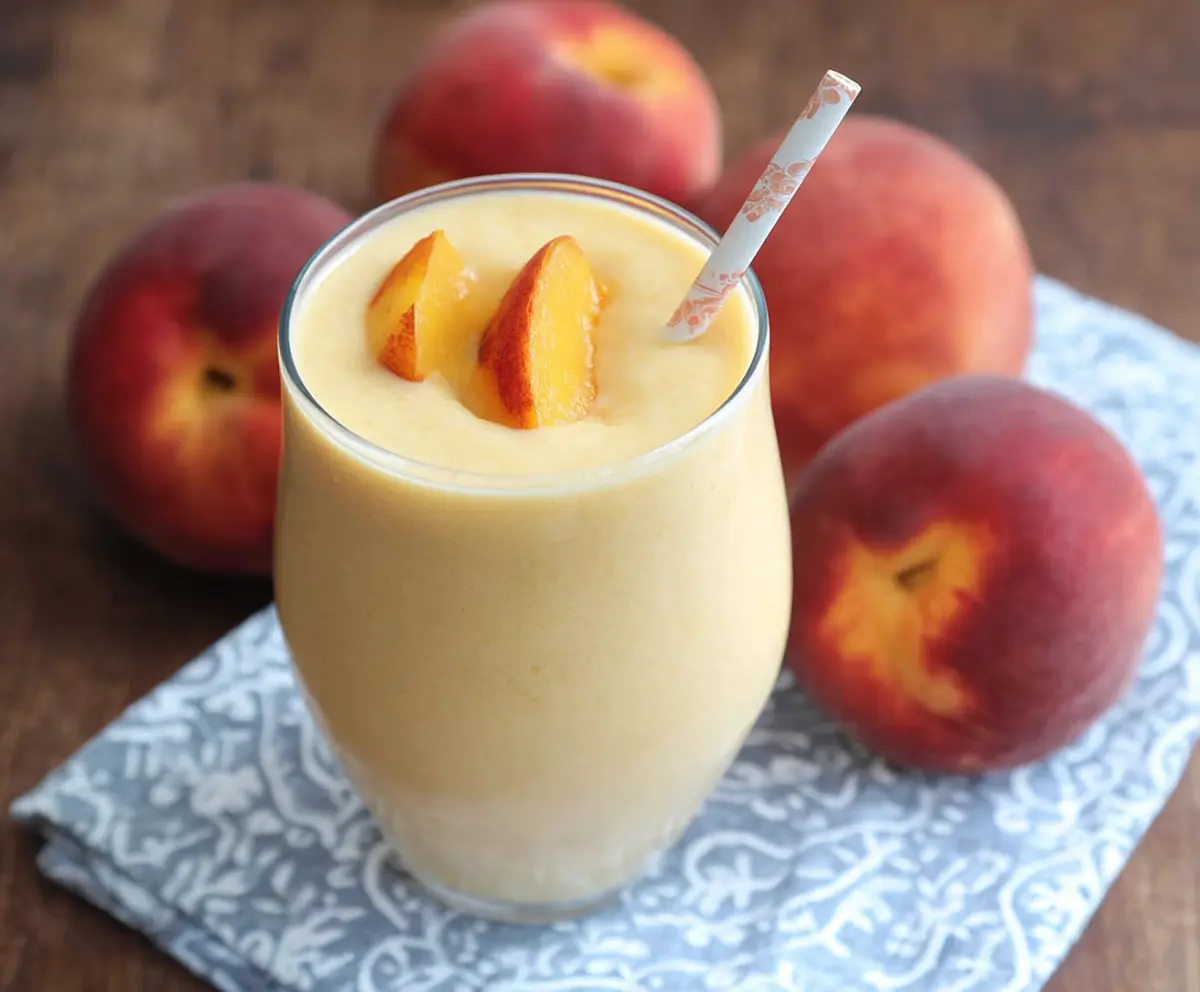Refreshing Peach Protein Smoothie in a glass with fresh peaches and ice cubes for a healthy breakfast.